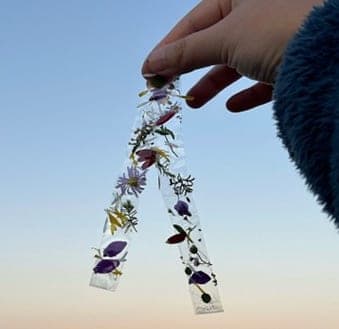 A hand holding up pressed-flower bookmarks against a clear evening sky