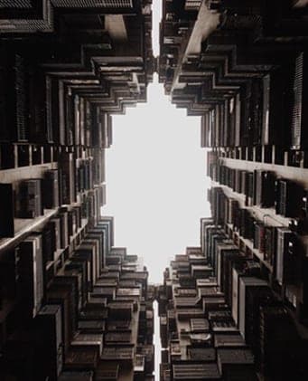 Looking up through a deep courtyard lined with stacked balconies towards a bright patch of sky