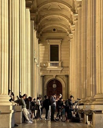 Visitors gathered beneath a tall colonnade of cream columns leading into a vaulted entrance hall