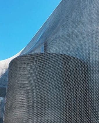 A curved building wrapped in perforated metal mesh against a blue sky